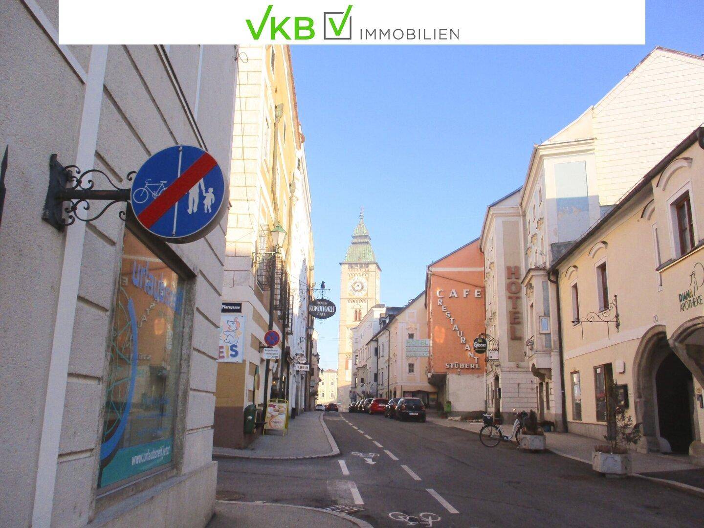 Blick die historische Gasse hinunter mit traditionellen Gebäuden und einem Kirchturm in der Ferne.