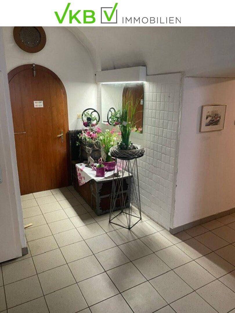 Eingangsbereich mit Fliesenboden, einer Holztür und einem dekorativen Tisch mit Pflanzen.