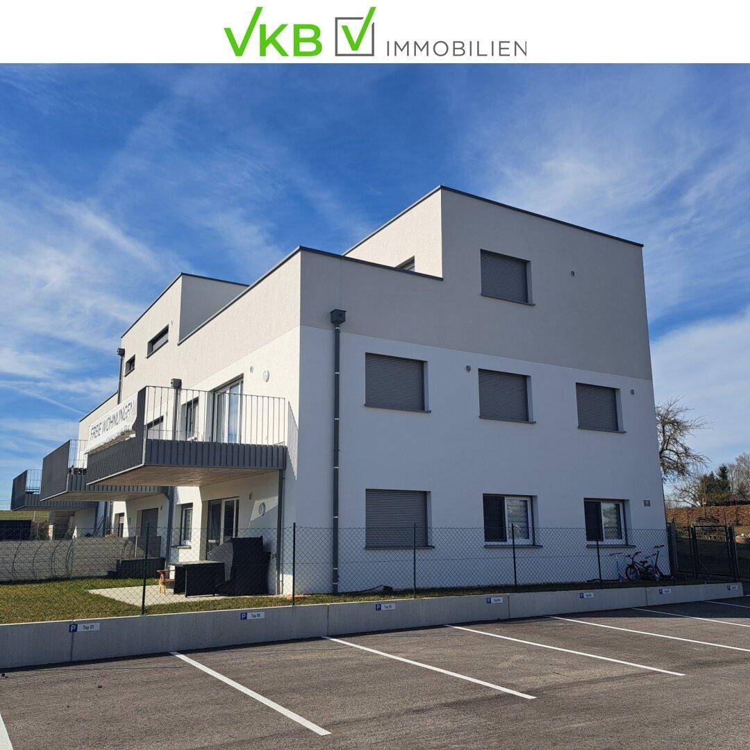 Rückansicht eines modernen Wohngebäudes mit Balkonen und zugehörigen Außenparkplätzen.