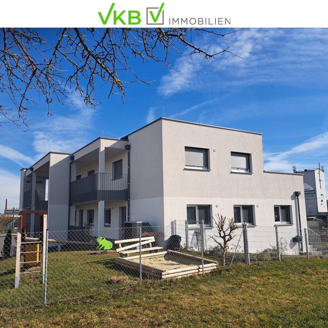 Ansicht eines modernen Neubaus mit weißer Fassade und einem Sandkasten im Gartenbereich.