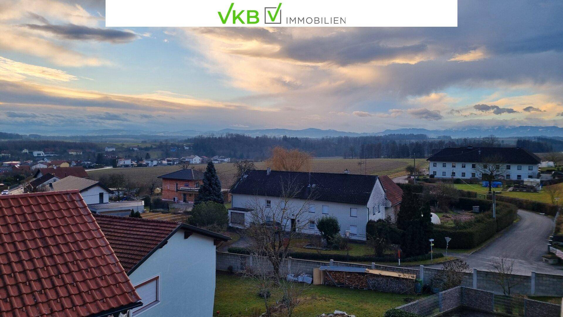 Weitläufige Aussicht über die ländliche Umgebung mit Häusern, Feldern und Bergen am Horizont.