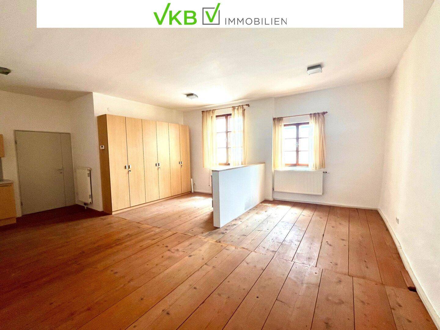 Geräumiger Innenraum mit breiten Holzdielen, großen Fenstern und einem praktischen Wandschrank.