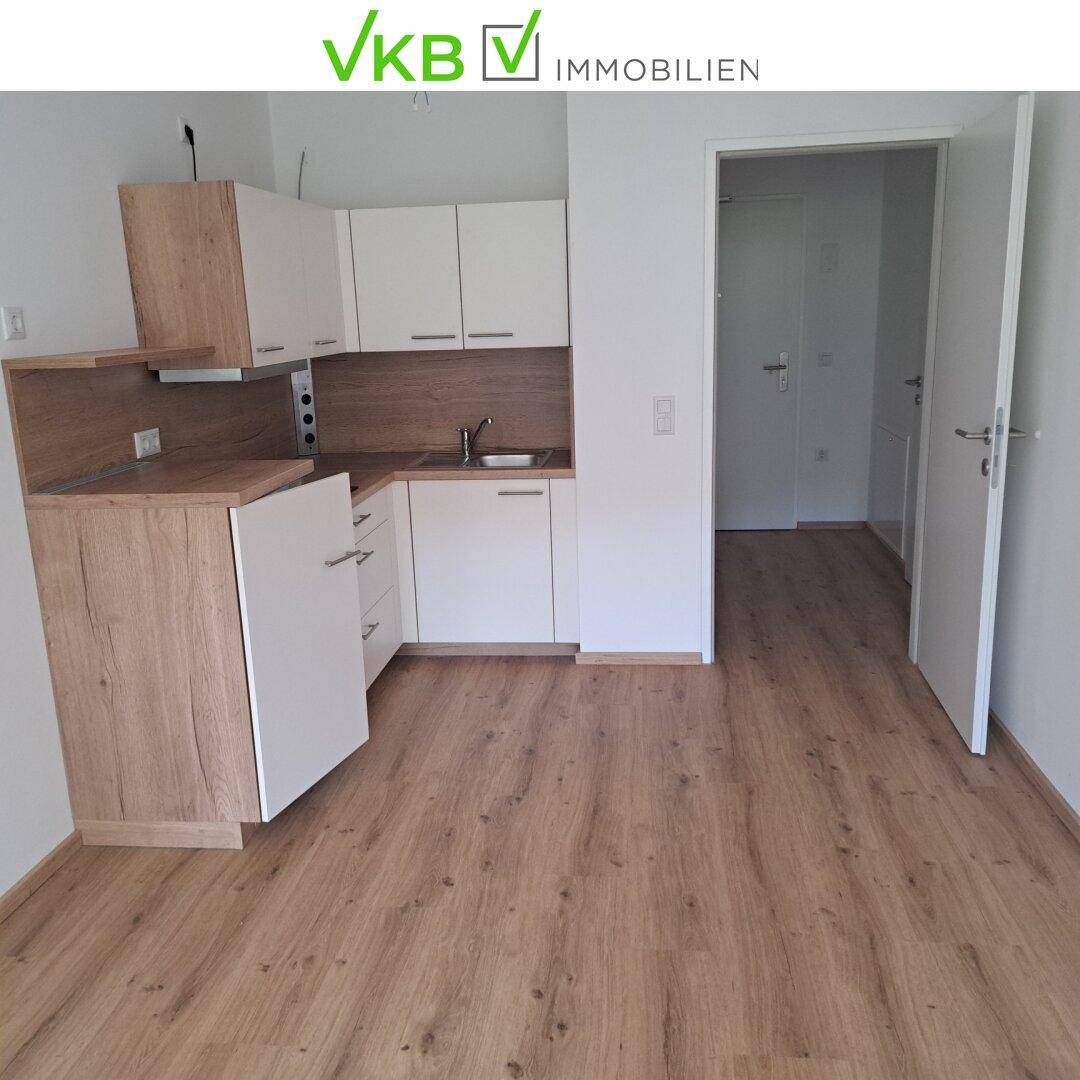 Kompakte Einbauküche mit hellen Holz- und weißen Fronten, offen zum Wohnbereich.