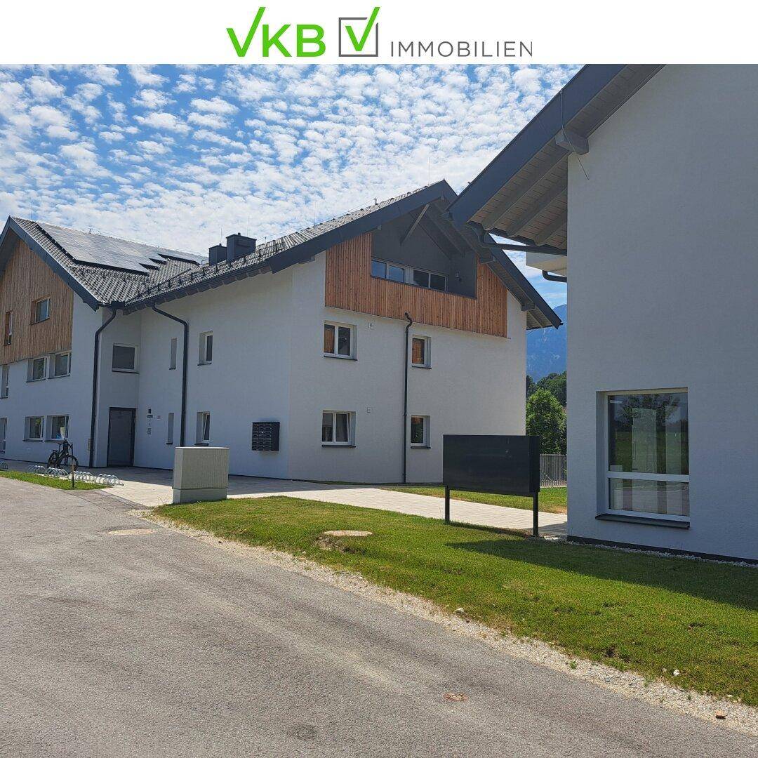 Moderne Wohnanlage mit weißer Fassade, Holzelementen und Photovoltaikanlage auf dem Dach.