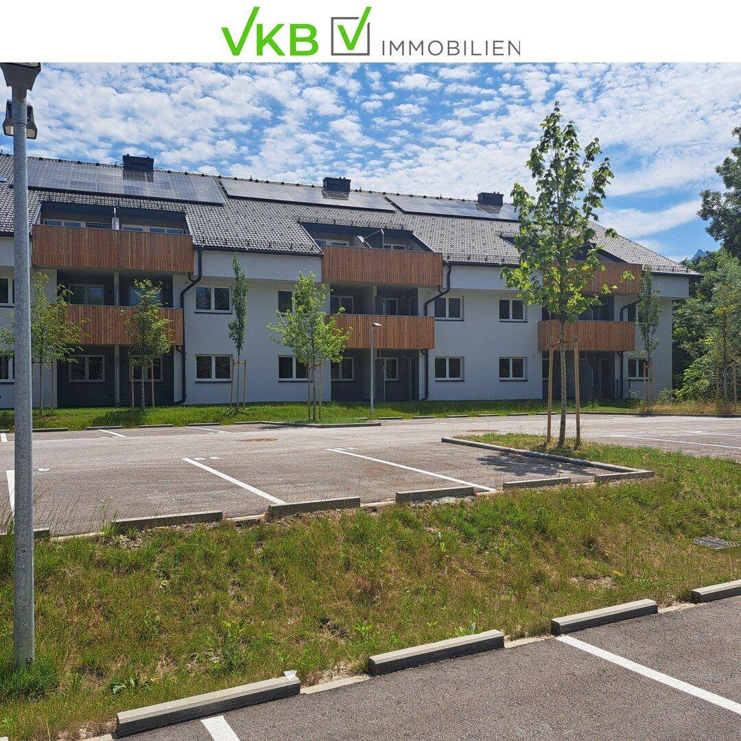 Mehrfamilienhaus mit Balkonen, Photovoltaikanlage und ausreichend Parkplätzen im Außenbereich.