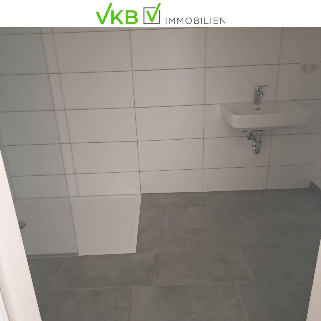 Modern gefliestes Badezimmer mit weißem Waschbecken und grauen Bodenfliesen.