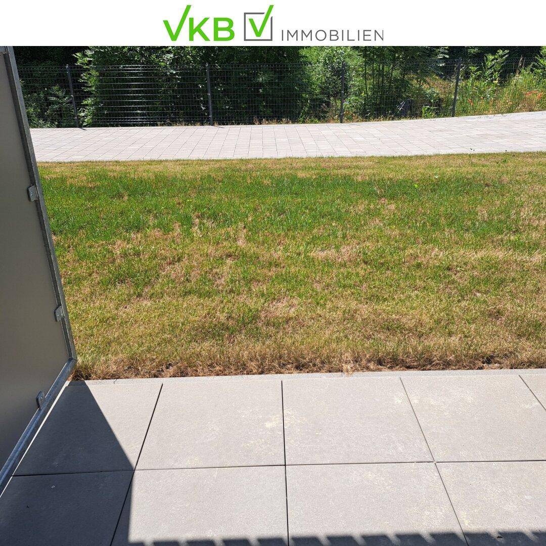 Grüner Rasenbereich direkt angrenzend an die Terrasse, umgeben von einem Zaun.