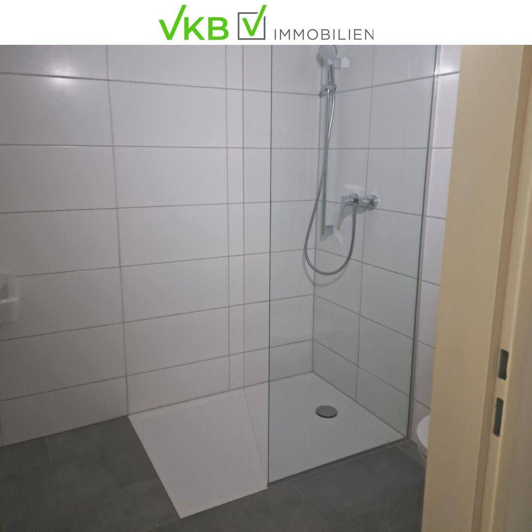 Modernes Badezimmer mit ebenerdiger Dusche und weißen Wandfliesen.