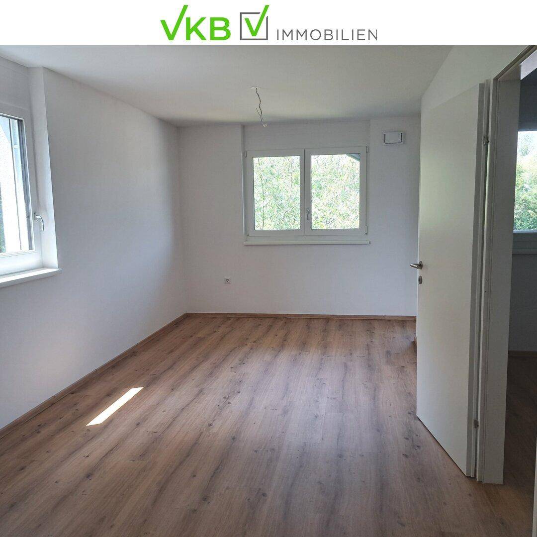Heller Raum mit Laminatboden und großen Fenstern, die viel Tageslicht hereinlassen.