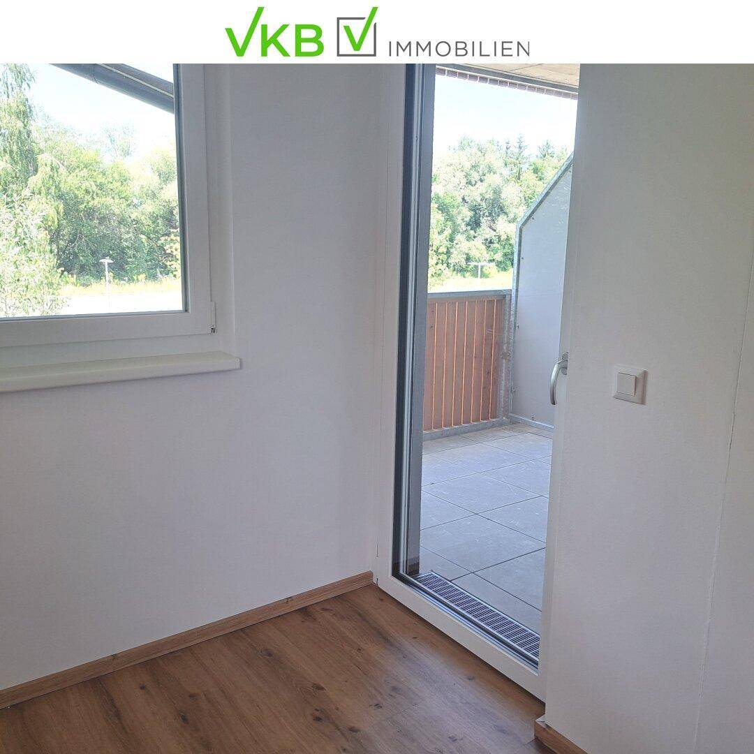Heller Raum mit Zugang zu einem Balkon, ausgestattet mit Laminatboden und großen Fenstern.