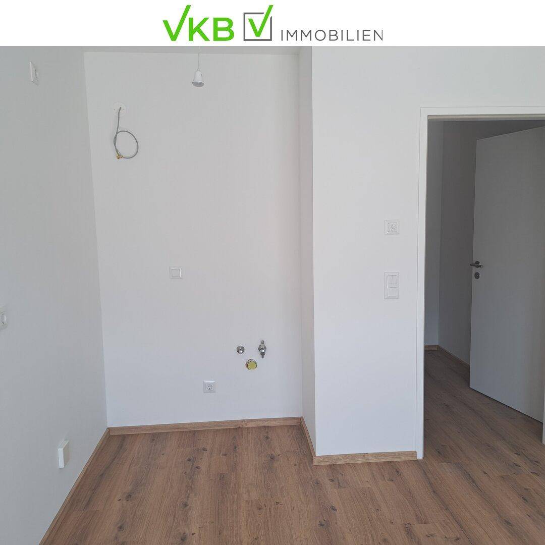 Leerer Raum mit Laminatboden und Anschlüssen für eine mögliche Küchenzeile oder Waschmaschine.