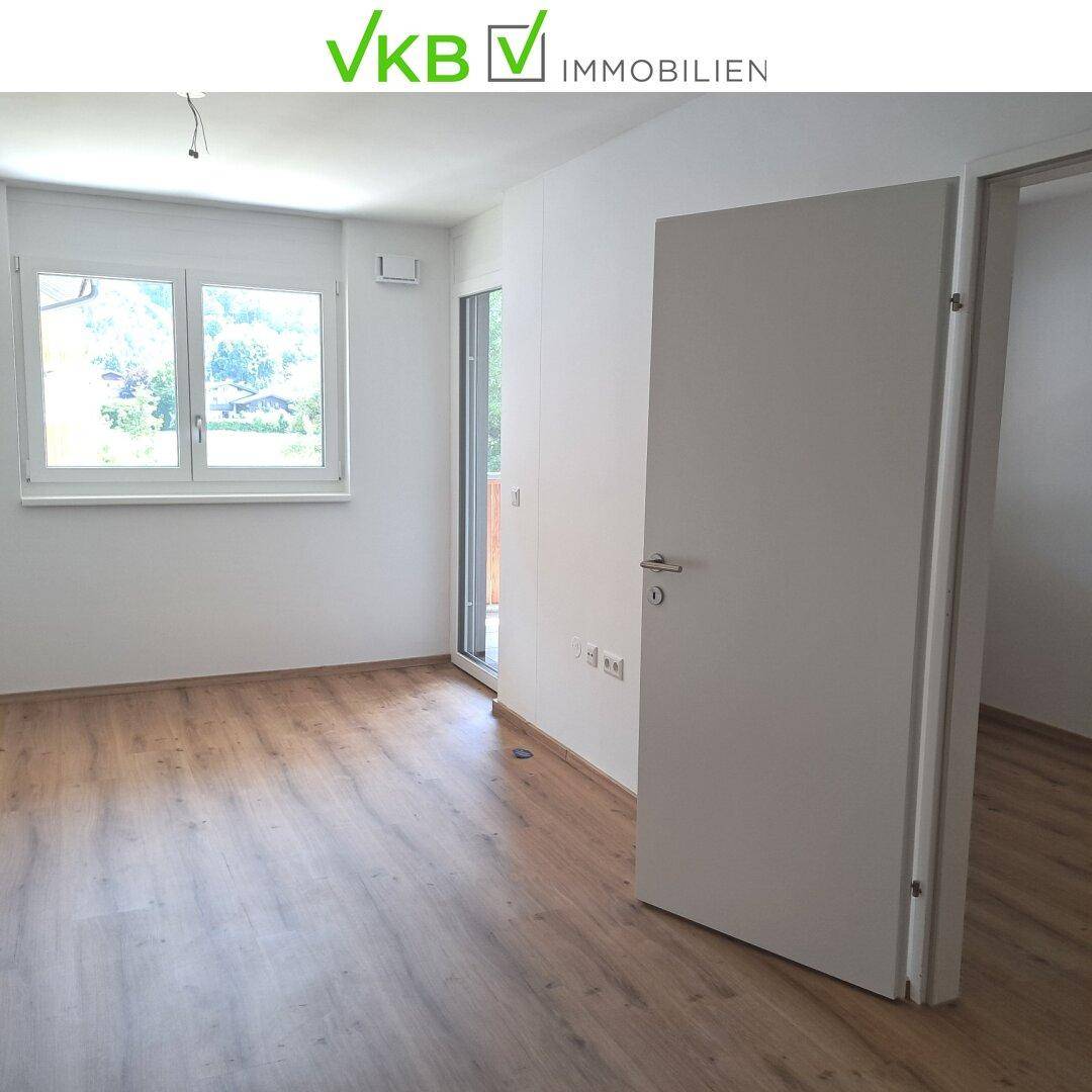Heller Wohnraum mit Laminatboden, großen Fenstern und Zugang zu einem Außenbereich.
