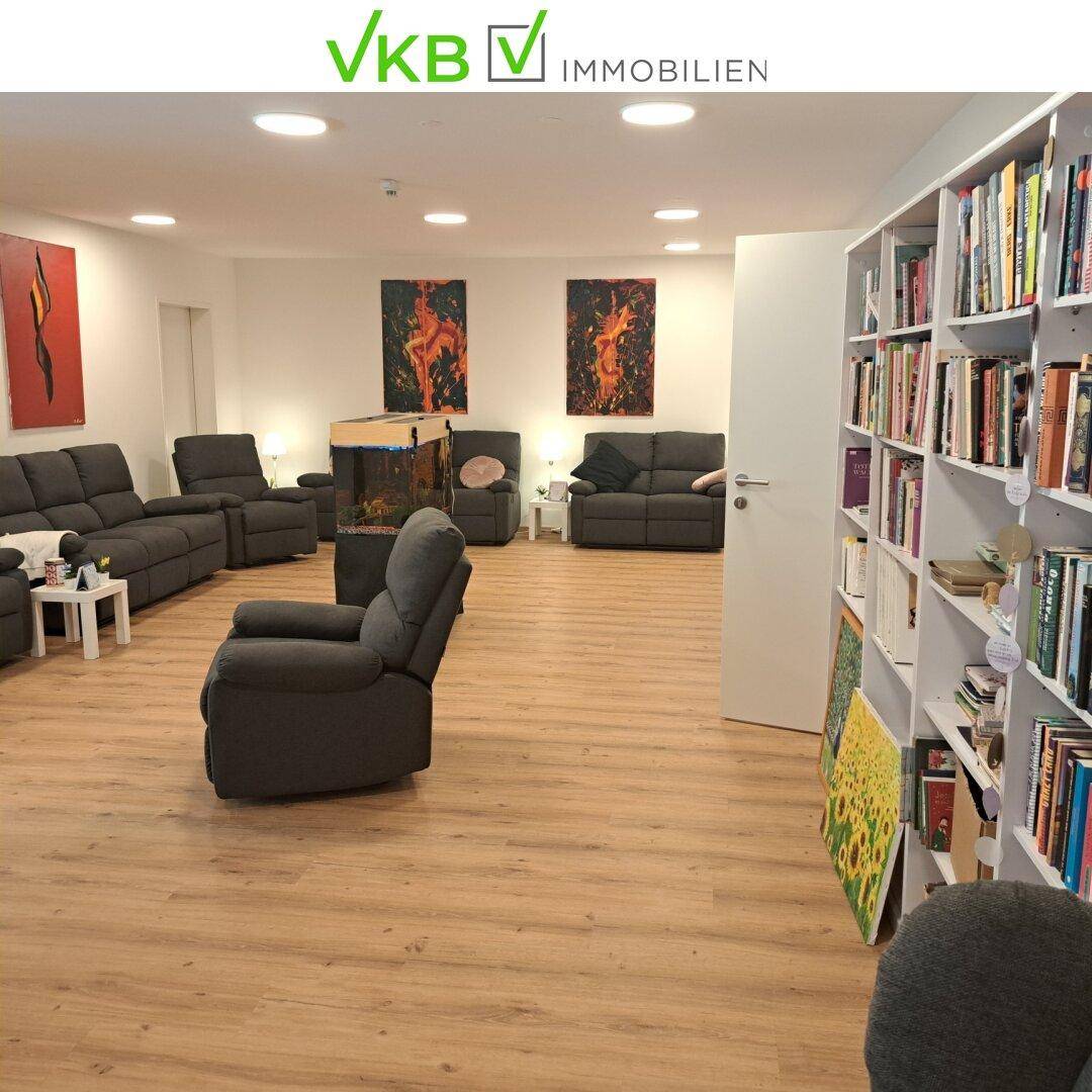 Geräumiger Gemeinschaftsraum mit bequemen Sofas, Bücherregalen und hellem Laminatboden.