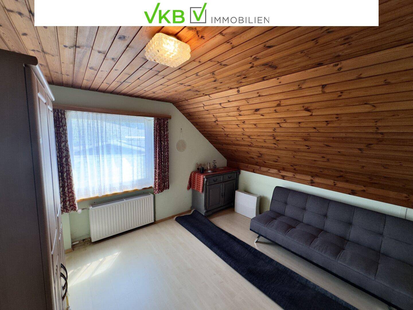 Gemütliches Dachzimmer mit Holzschrägen, Laminatboden und einem Fenster, ideal als Schlaf- oder Gästezimmer.