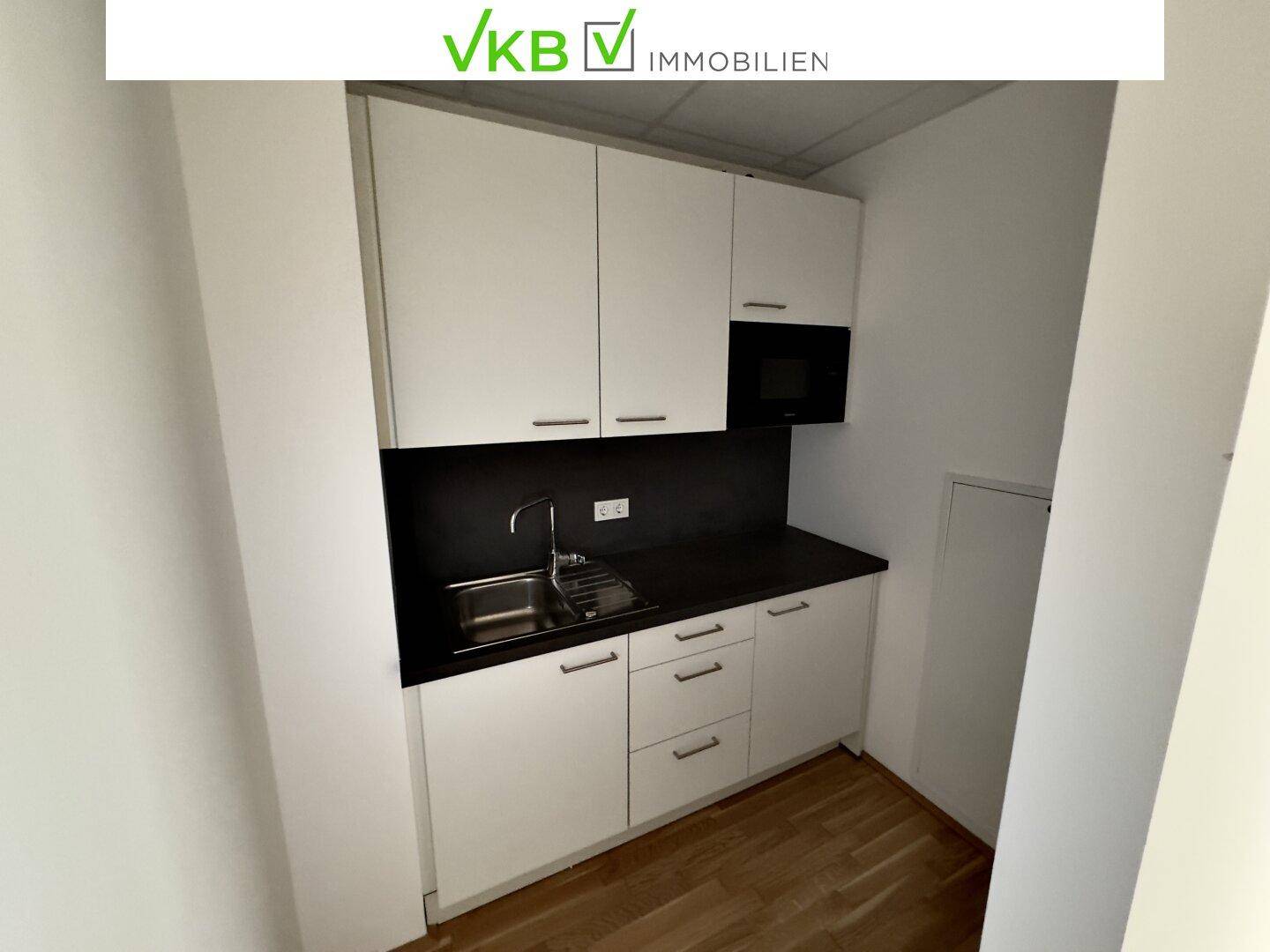 Kleine Einbauküche mit weißen Schränken, Spüle und integrierter Mikrowelle.