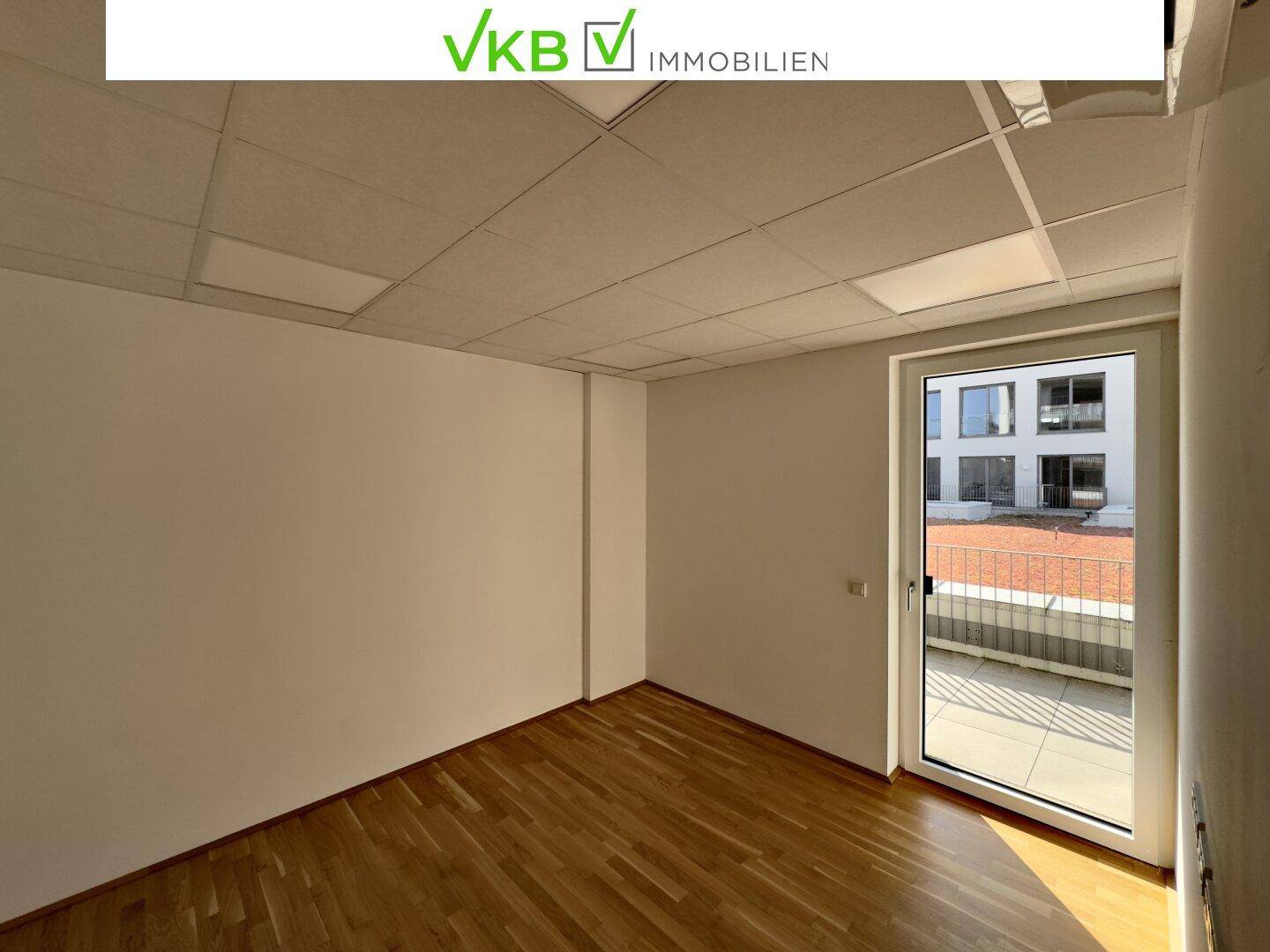 Leerer Büroraum mit Holzfußboden und großem Fenster, das viel Tageslicht hereinlässt.