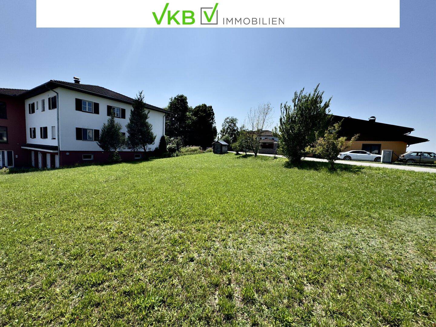 Große Rasenfläche mit Blick auf ein Mehrfamilienhaus und weitere Gebäude in der Ferne an einem sonnigen Tag.