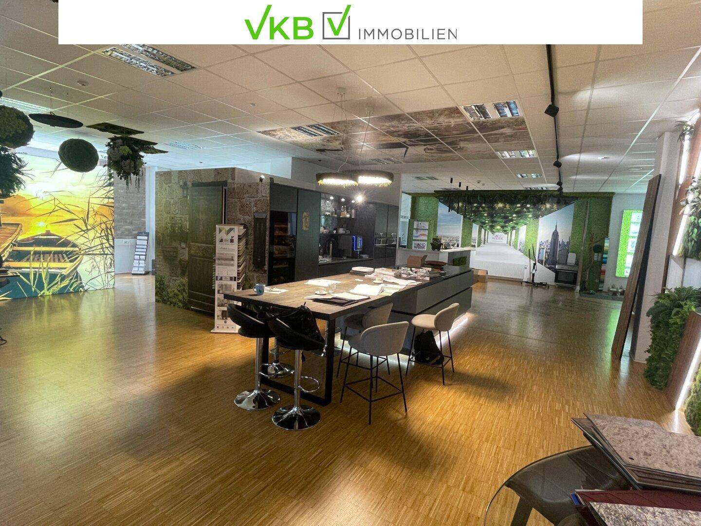 Offener Bürobereich mit großem Besprechungstisch, Barhockern und einer integrierten Küchenzeile.