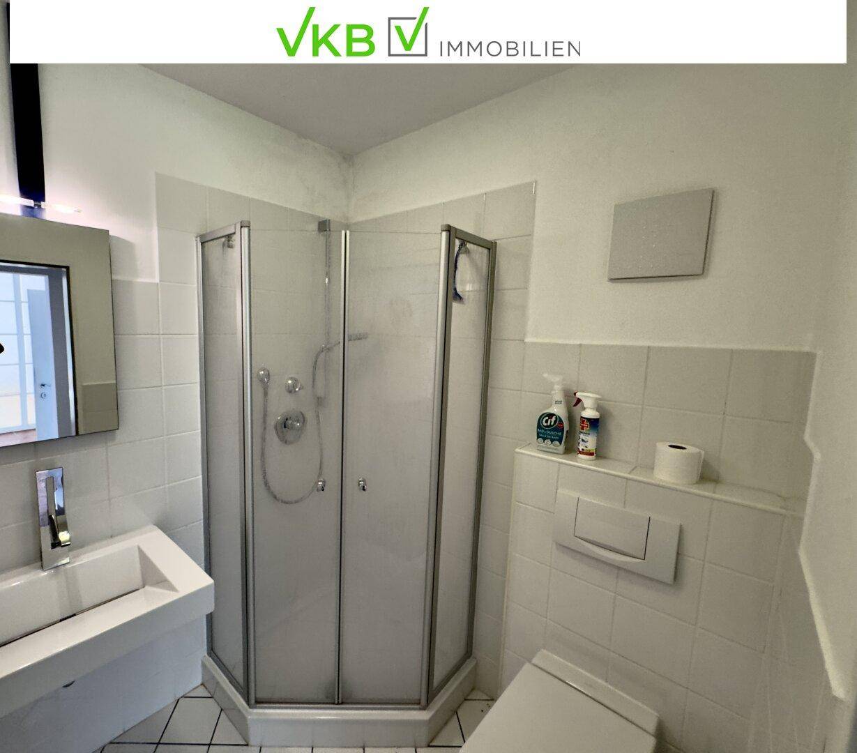 Helles Badezimmer mit Eckdusche, weiß gefliesten Wänden und modernem Waschbecken.