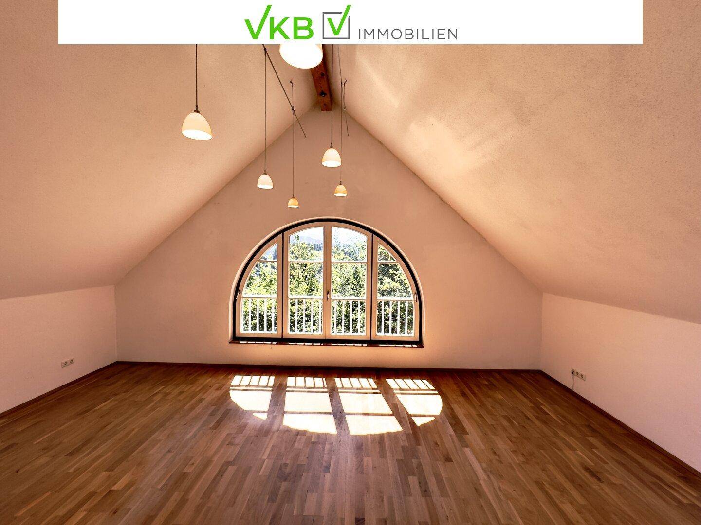 Geräumiger Raum im Dachgeschoss mit Holzboden und einem beeindruckenden Rundbogenfenster.