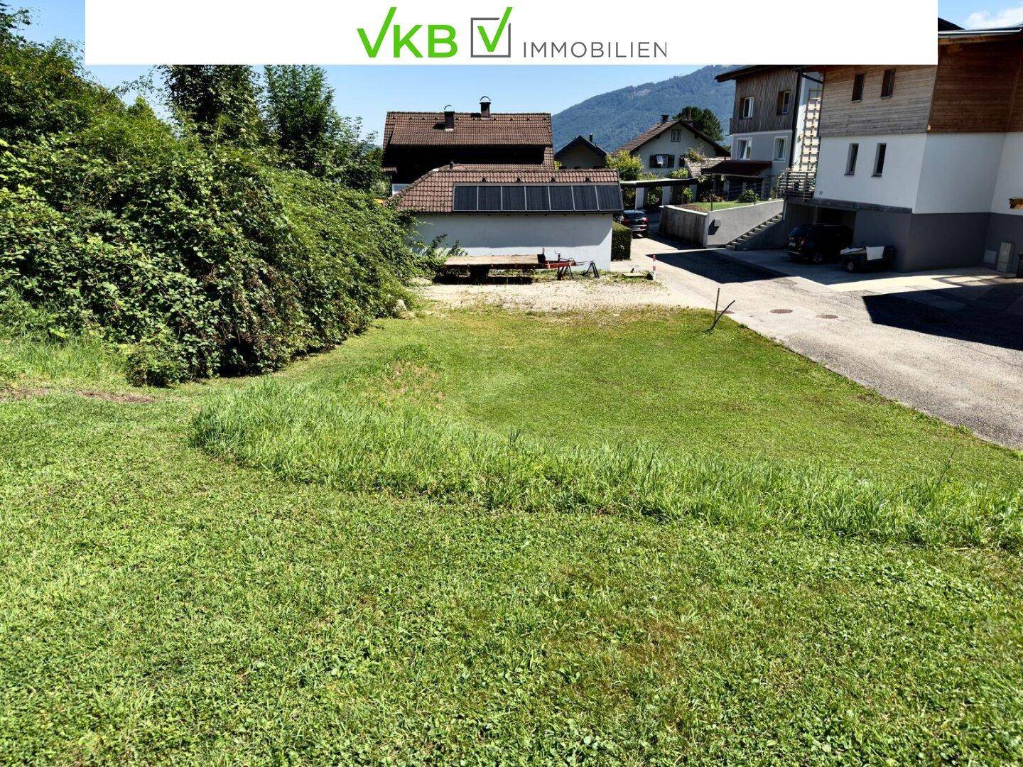 Grünes Grundstück mit angrenzenden Häusern und einem Gebäude mit Photovoltaikanlage.