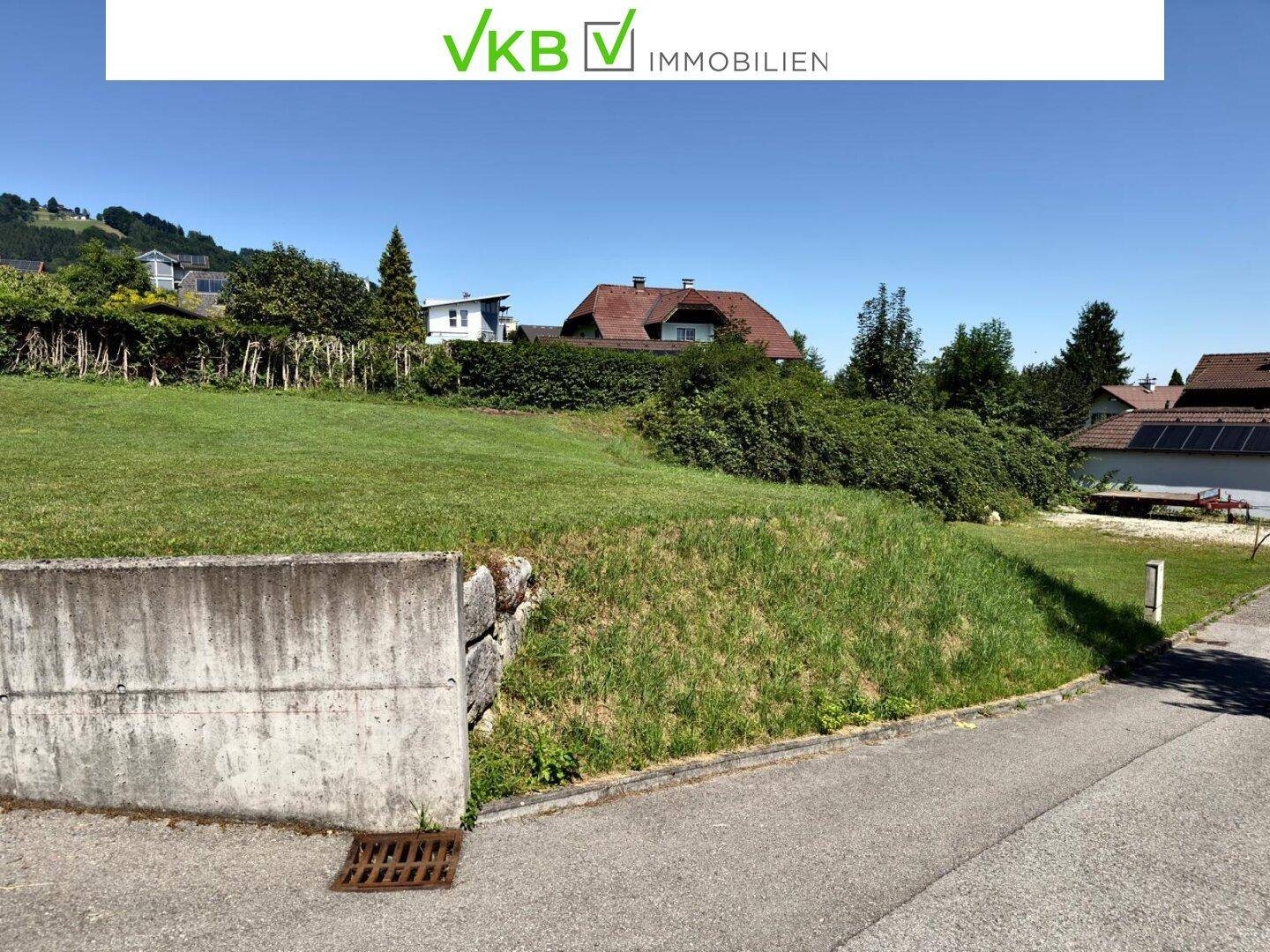 Grüne Hanglage des Grundstücks neben einer Straße mit Blick auf weitere Wohnhäuser.