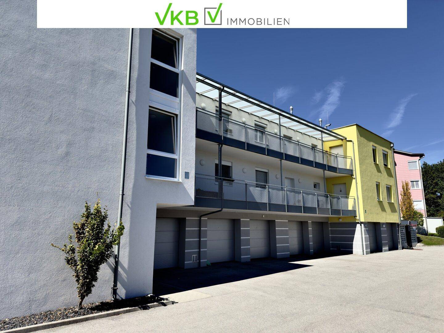 Ansicht des modernen Wohngebäudes mit Balkonen, Garagen und einer hellgelben Fassade.
