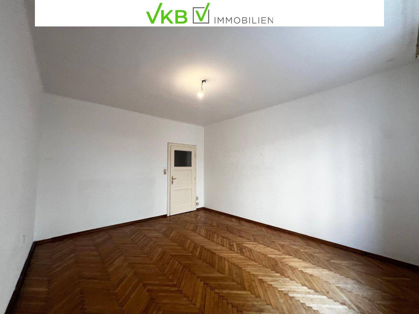 Helles Zimmer mit klassischem Fischgrätparkett und einer Tür, bereit zur individuellen Gestaltung.