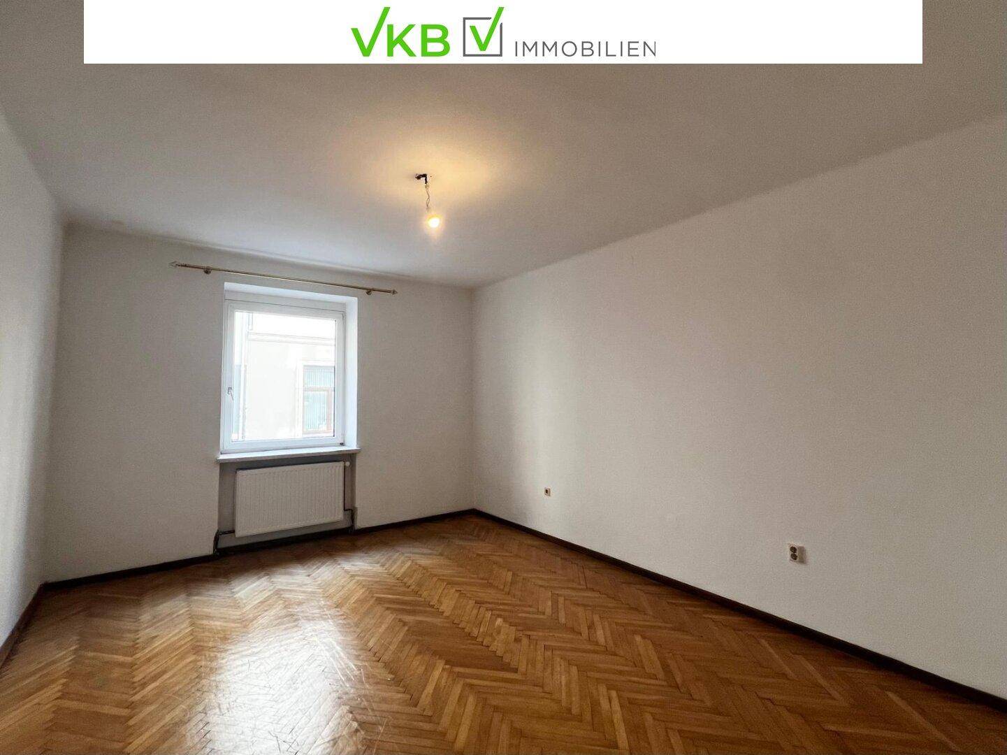 Geräumiges Zimmer mit Fischgrätparkett, weißen Wänden und einem Fenster mit Heizkörper.