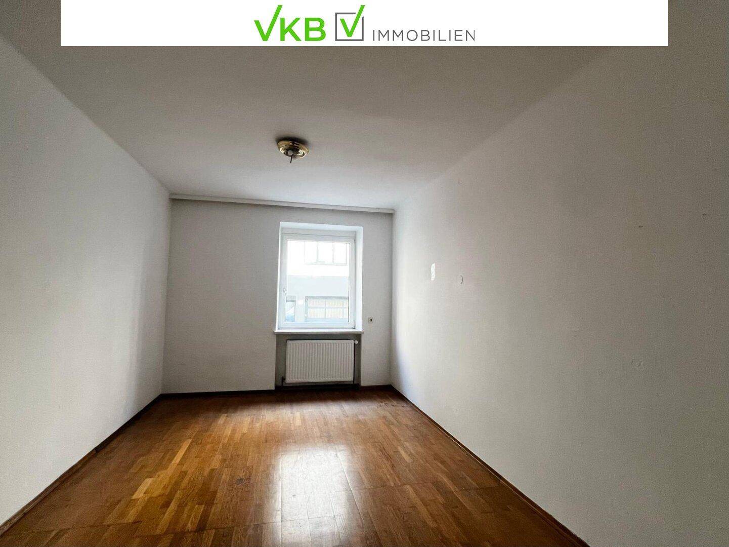 Freundliches Zimmer mit Dielenboden, weißen Wänden und einem Fenster, das viel Licht hereinlässt.