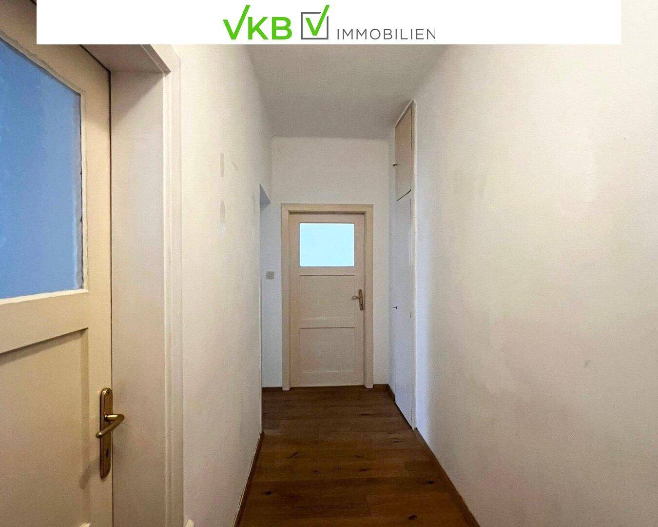 Heller Flur mit Holzboden und weißen Wänden, der zu weiteren Räumen führt.