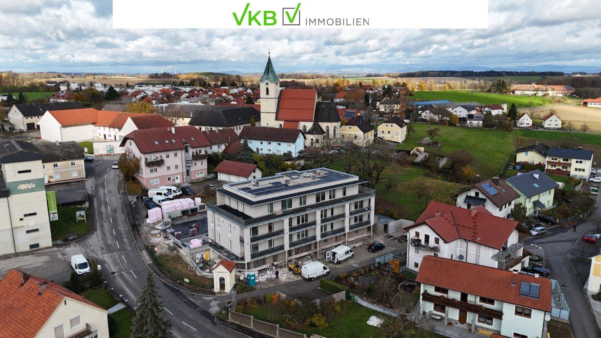 Weitwinkel-Luftaufnahme des neuen Gebäudes eingebettet in die ländliche Umgebung mit Kirche und Wohnhäusern.
