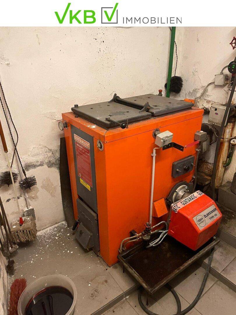 Heizungsraum im Keller mit einem großen, orangefarbenen Heizkessel und einfacher, funktionaler Ausstattung.