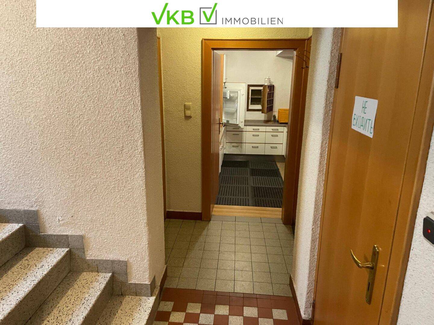 Flur mit Fliesenboden und Blick in eine angrenzende Küche, die durch eine Tür zugänglich ist.