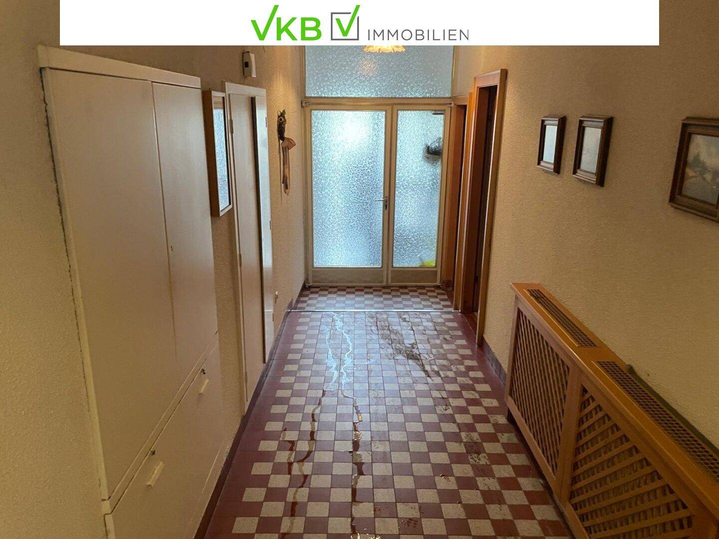 Langer Flur mit kariertem Fliesenboden, weißem Wandschrank und einer verglasten Eingangstür, traditionell eingerichtet.