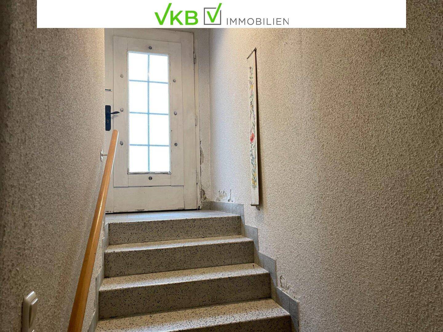 Treppenaufgang mit Terrazzoboden und Holzgeländer, der zu einer weiteren Etage des Hauses führt.