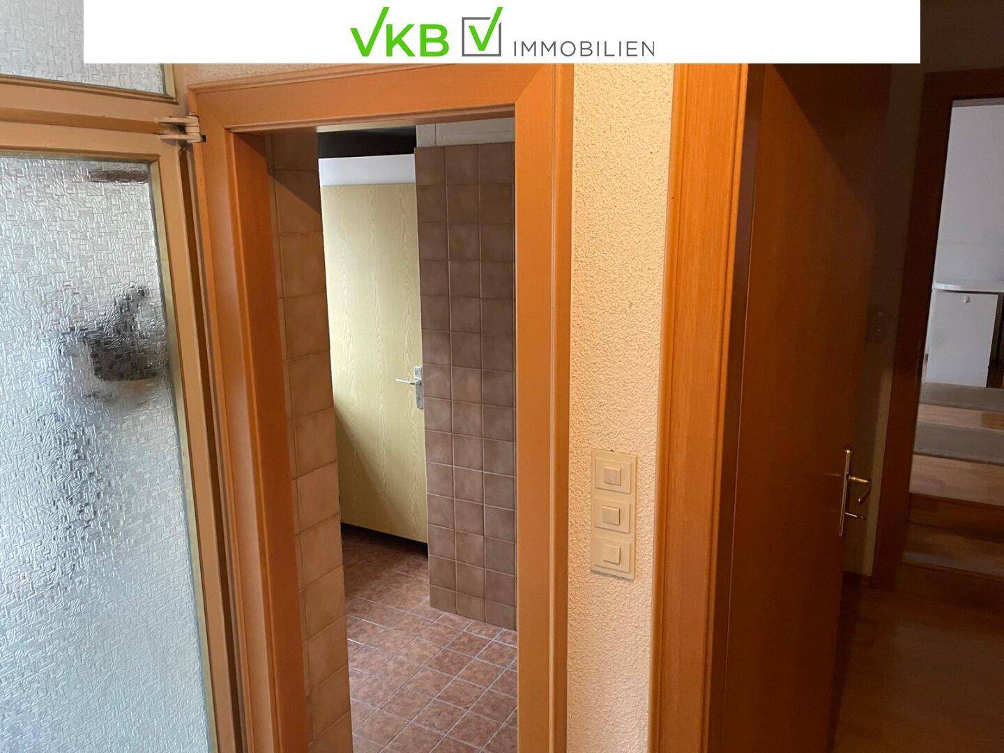 Schmaler Flur mit Blick in einen gefliesten Raum, möglicherweise ein Badezimmer oder eine Abstellkammer.