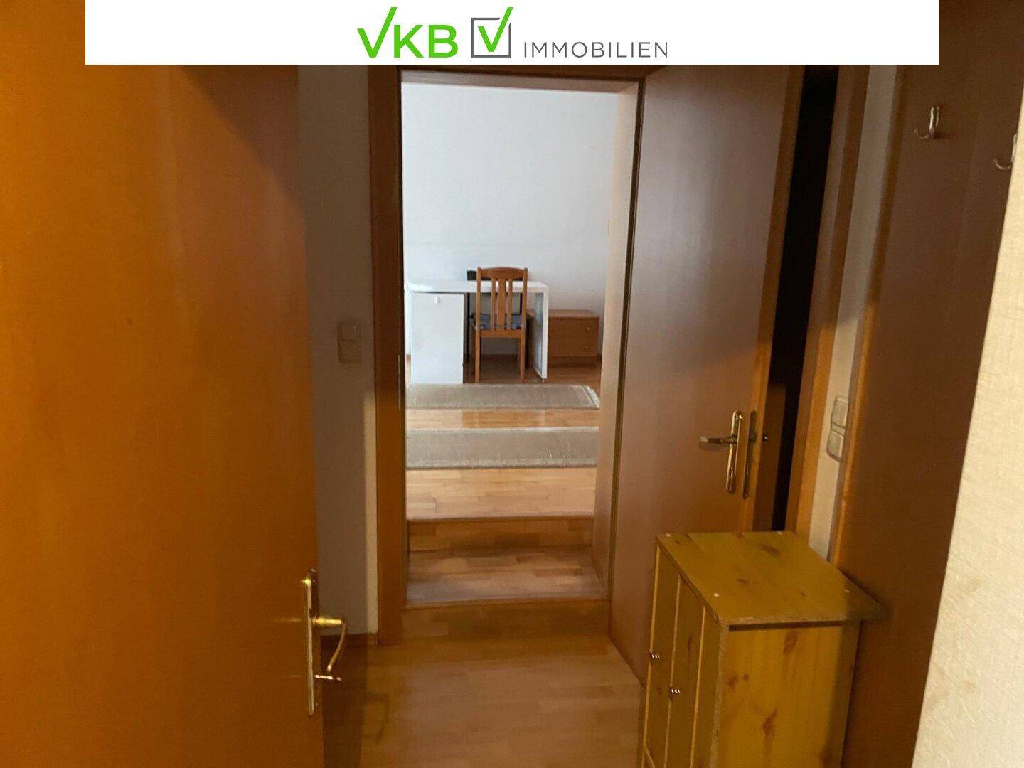 Schlichter Flur mit Holzboden, der zu einem weiteren Zimmer mit Schreibtisch und Stuhl führt.