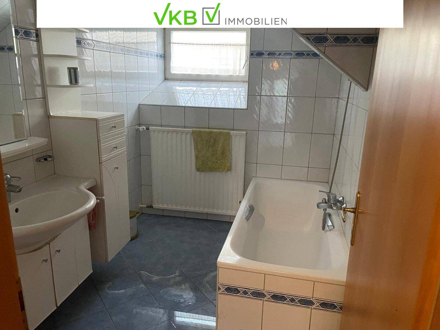 Badezimmer mit blauen und weißen Fliesen, Badewanne, Waschbecken und Fenster, funktional ausgestattet.