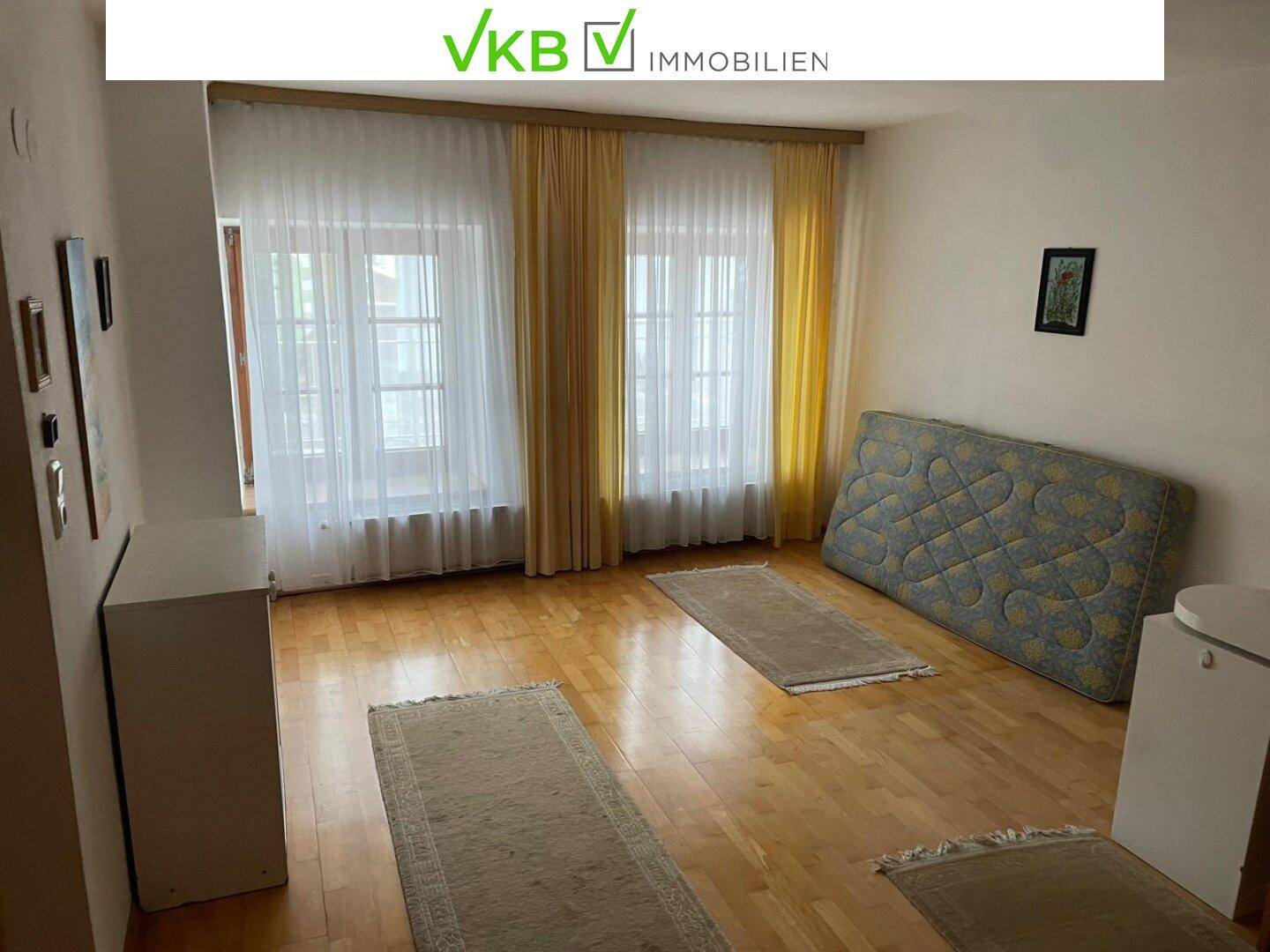 Helles Zimmer mit Holzboden, zwei Fenstern und einem Matratzenlager, das als Schlafzimmer dient.