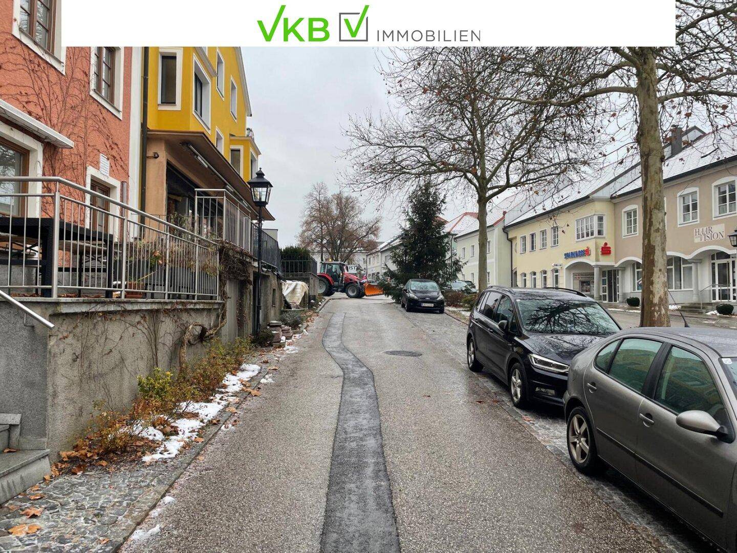 Blick auf eine verschneite Straße mit parkenden Autos und angrenzenden Gebäuden in einer Wohngegend.