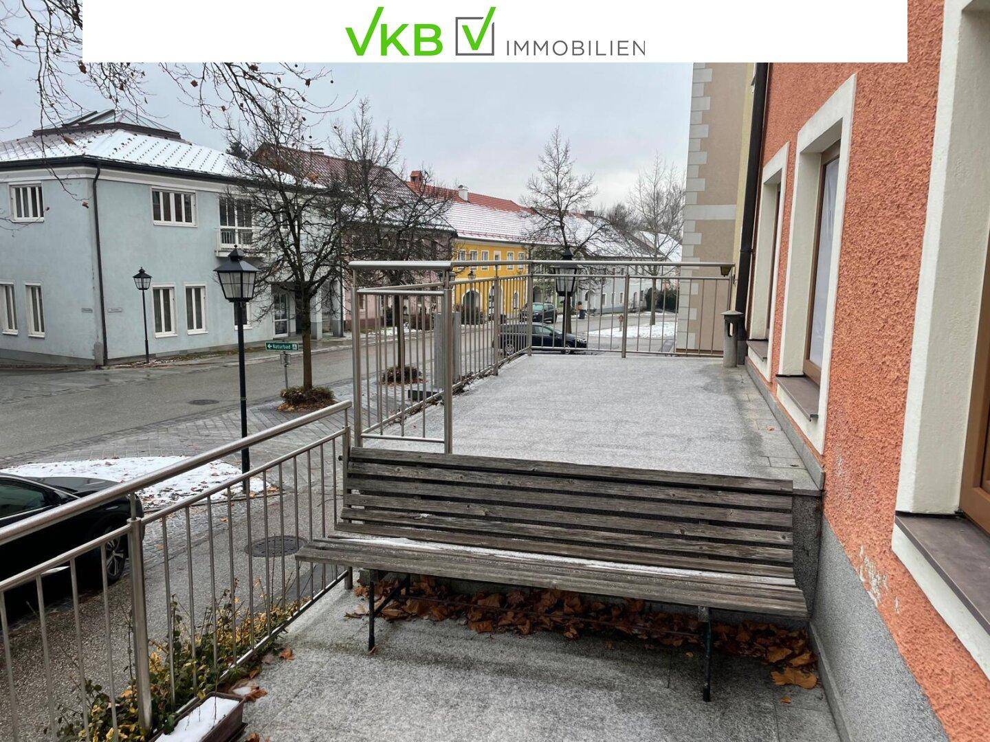 Große Außenterrasse mit Metallgeländer und einer Holzbank, bedeckt mit leichtem Schnee und Blick auf die Straße.
