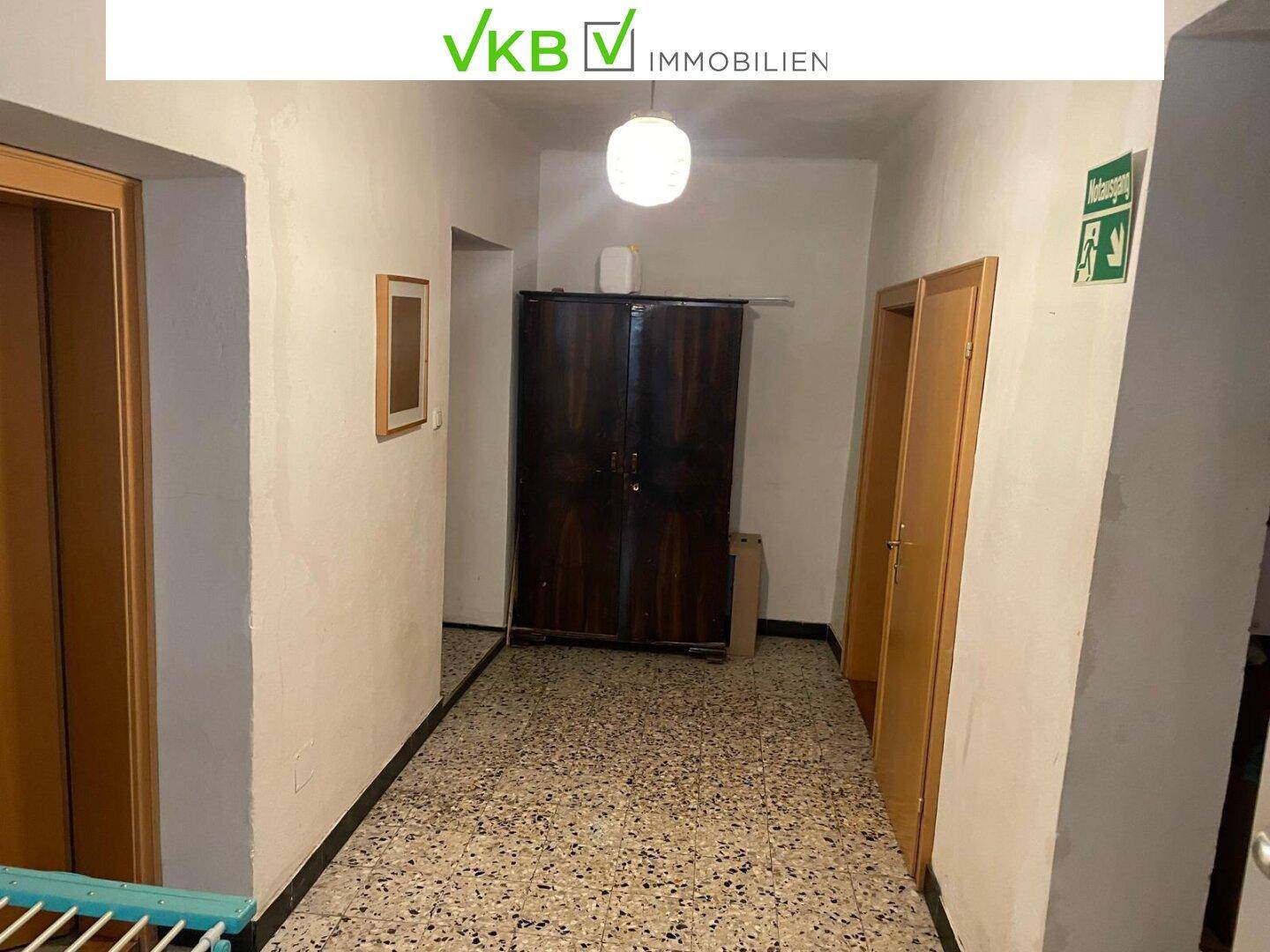 Schlichter Flur mit Terrazzoboden und einem dunklen Schrank, der zu weiteren Zimmern führt.