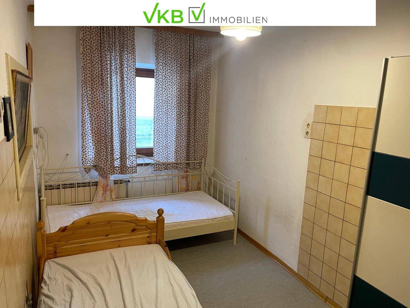 Schlafzimmer mit zwei Einzelbetten, Fenster und einem Kleiderschrank, einfach und funktional eingerichtet.