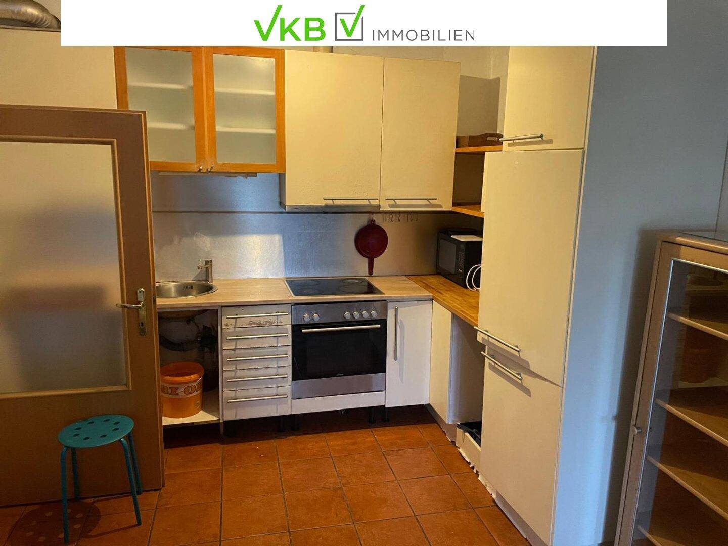 Einfache Küche mit beigen Schränken, Spüle, Herd und Mikrowelle, funktional ausgestattet.