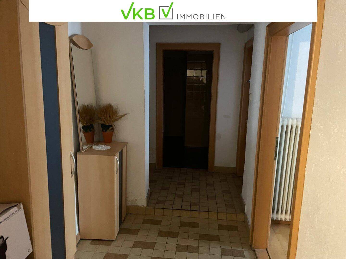 Flur mit Fliesenboden und einem kleinen Schrank, der zu weiteren Räumen führt.