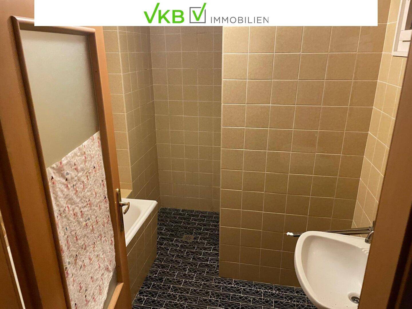 Badezimmer mit beigen Fliesen, Badewanne und Waschbecken, einfach und funktional ausgestattet.
