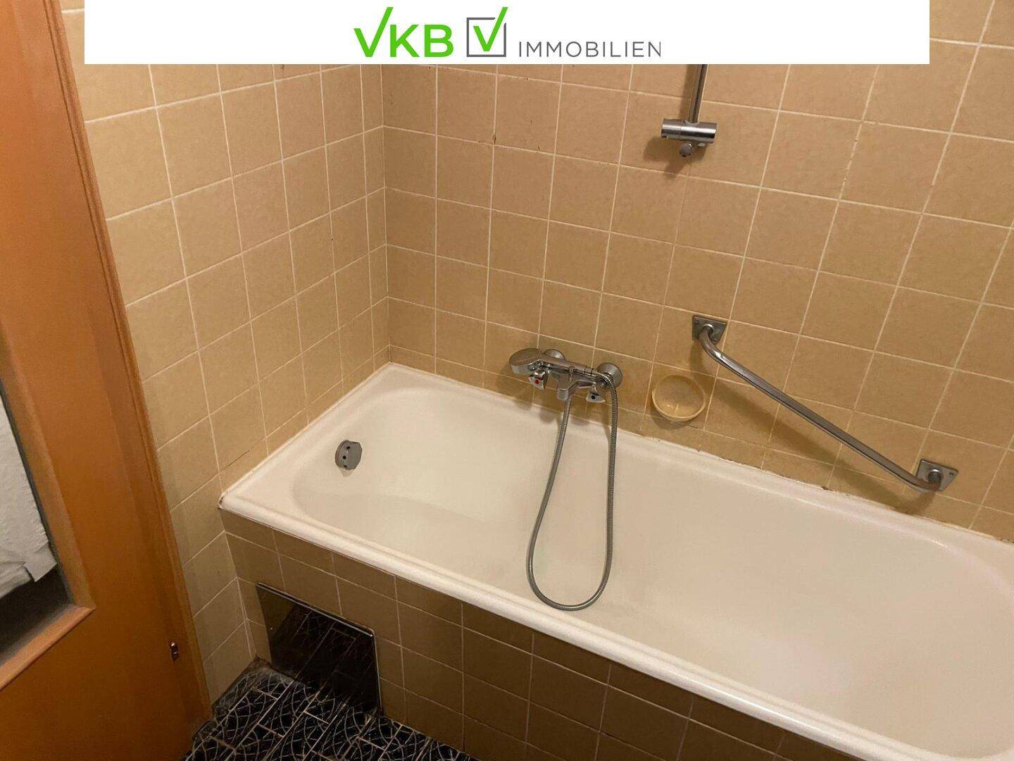 Badezimmer mit Badewanne und Haltegriff, umgeben von beigen Fliesen, einfach ausgestattet.