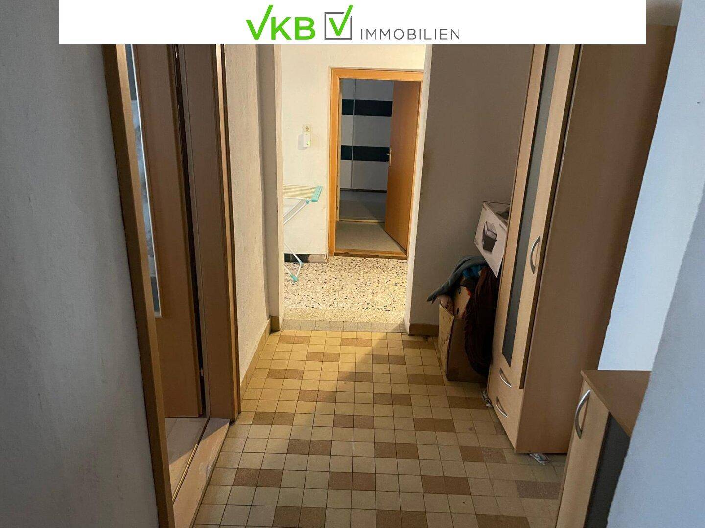 Flur mit Fliesenboden und Schränken, der zu weiteren Räumen und einem Treppenaufgang führt.