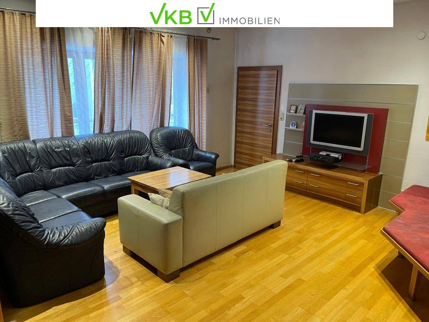 Geräumiges Wohnzimmer mit Holzboden, Ledersofas und einem Fernseher, modern und komfortabel eingerichtet.